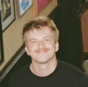a handsome young man with a mustache smiles at the camera: timo